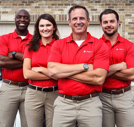 Four happy HomeTeam inspectors with folded arms and standing in front of a garage door